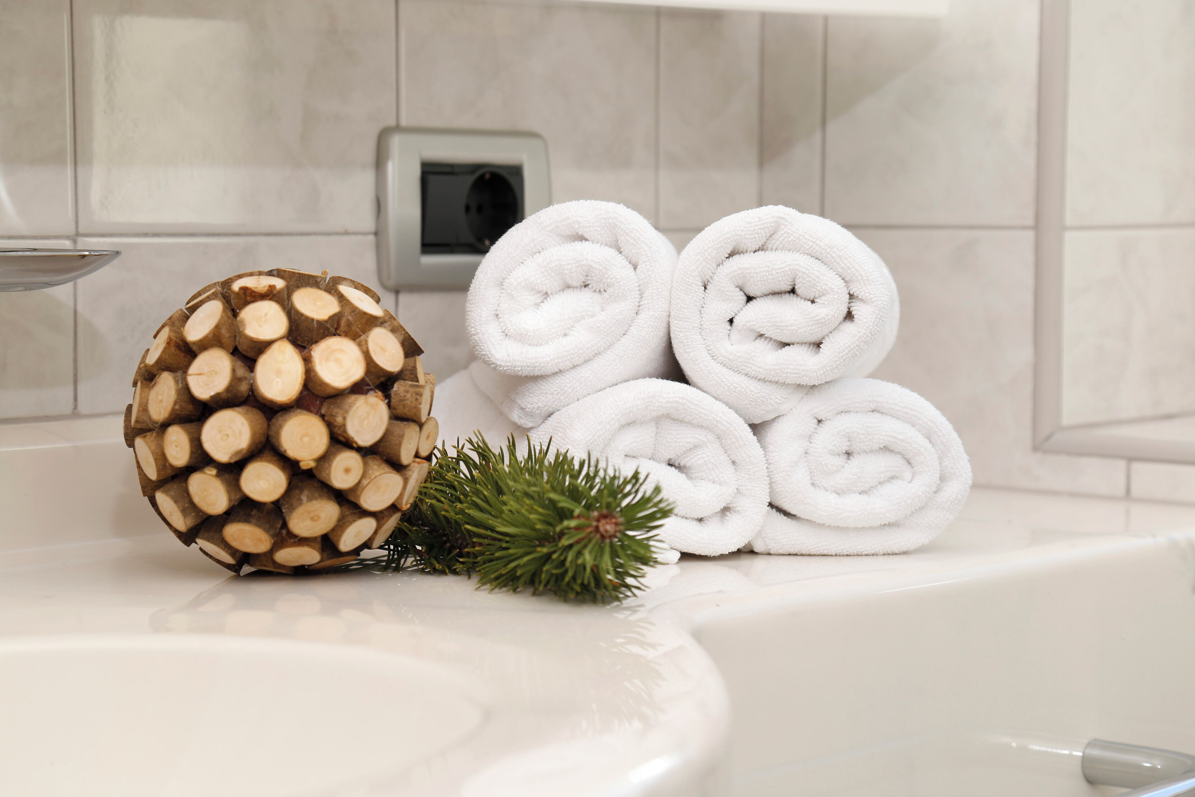 A bathroom with a white bathtub, a pine cone, and rolled white towels.