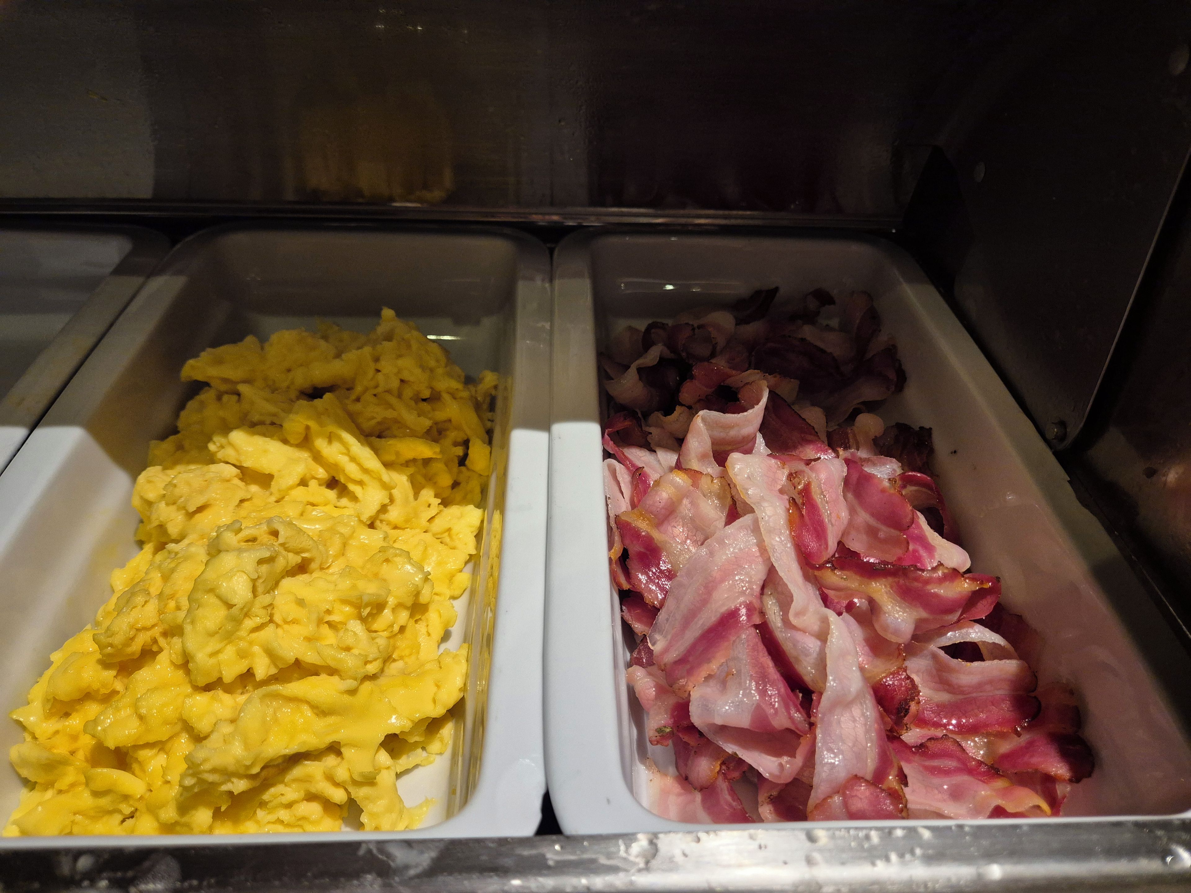 Dos dispensadores de comida con huevos revueltos y tocino.