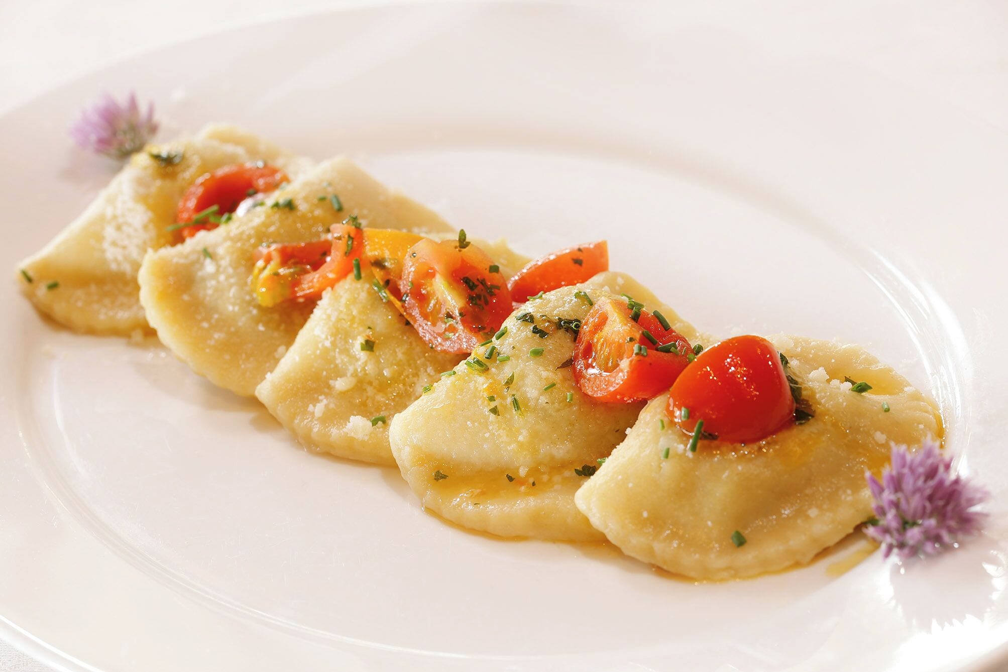 A plate of ravioli with a garnish of herbs and cherry tomatoes.