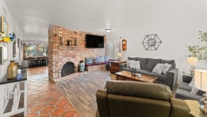 Un salón con chimenea de ladrillo, un sofá gris, una mesa de centro y piso de piedra.
