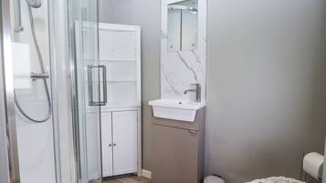 Ein modernes Badezimmer mit einer gläsernen Duschkabine, einem weißen Waschtisch mit Marmorablage und einem kleinen runden Hocker.