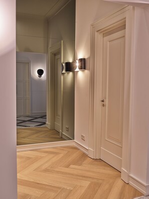A hallway with wooden flooring, white walls, and a door with a light switch. - Townhouse by THE QVEST (Cologne)
