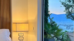 Habitación de hotel con cama, lámpara, vista de un paisaje urbano a través de un ventanal grande y una planta en maceta.