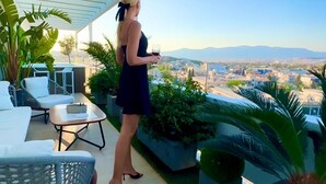 Una mujer parada en un balcón con vistas a la ciudad, sosteniendo una copa de vino.