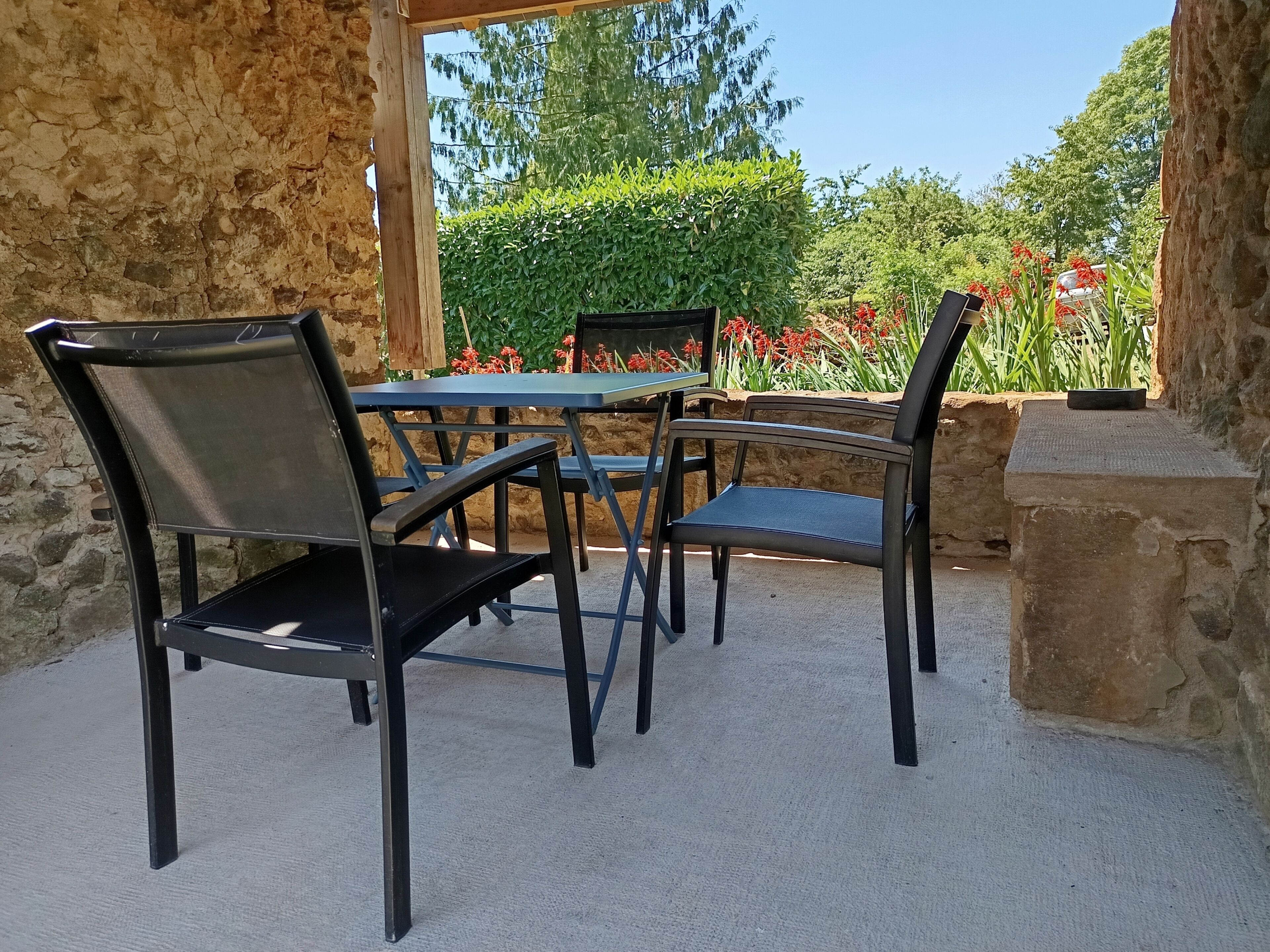 Un patio al aire libre con un muro de piedra, una mesa y cuatro sillas.