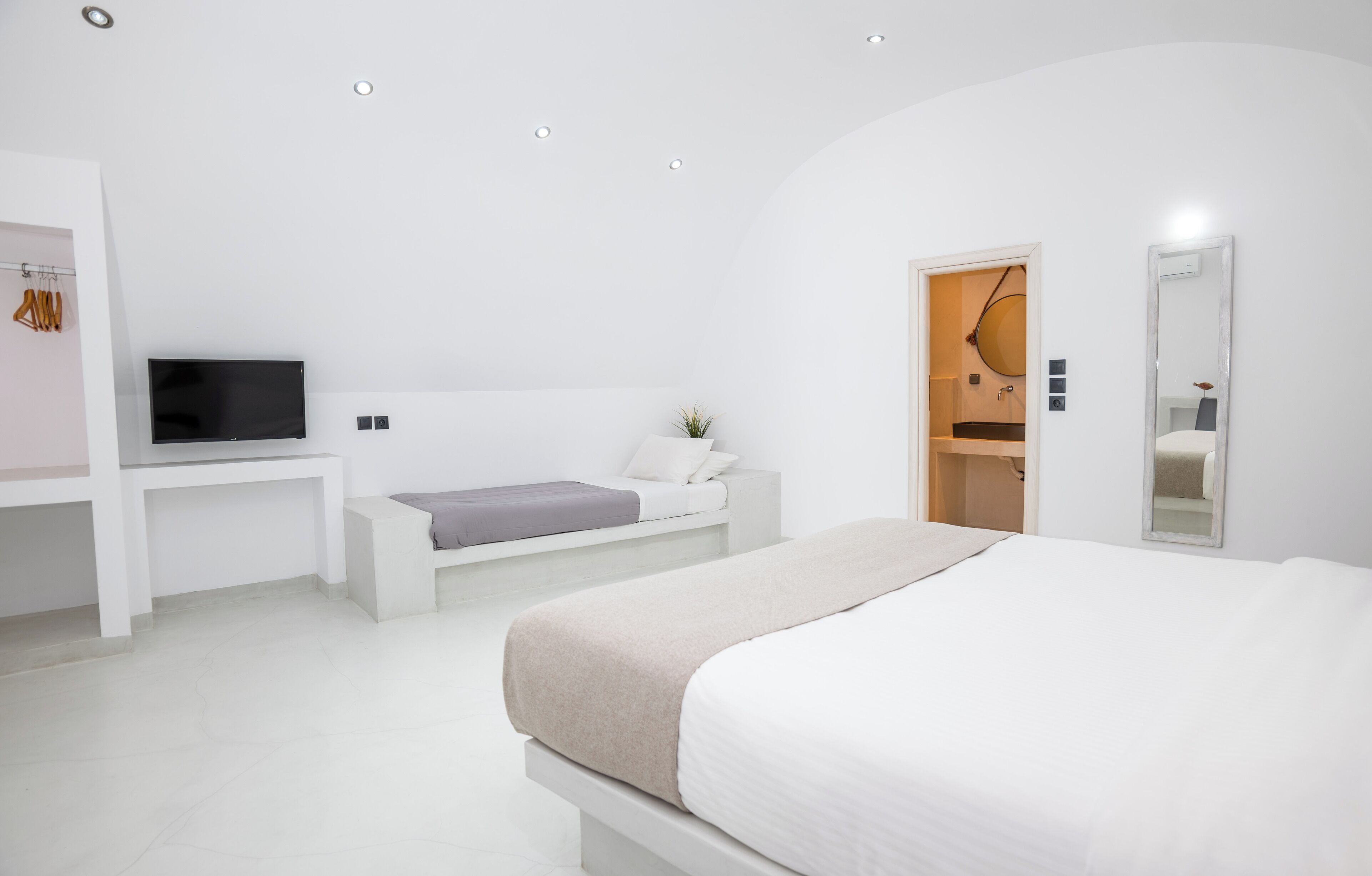 A modern hotel room with a large bed, a flat-screen TV, a bedside table, and a walk-in closet.
