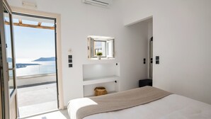 Un dormitorio con cama, ventana con vista al mar, espejo y repisa con una planta.