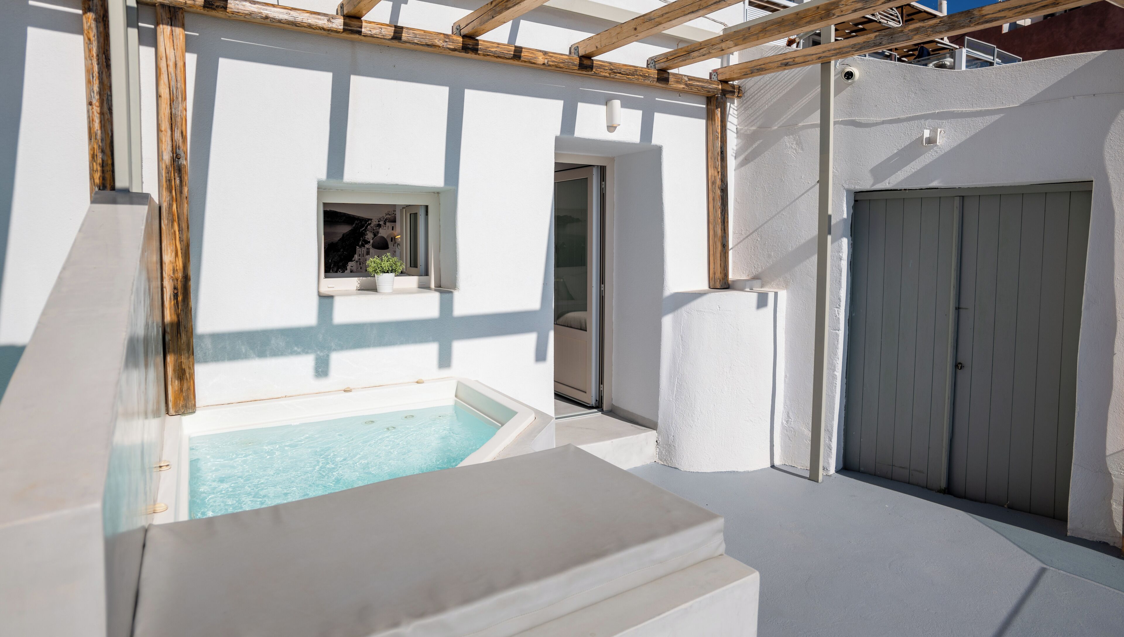 A modern outdoor pool area with a clear view of the pool, a wooden pergola, and a white door.