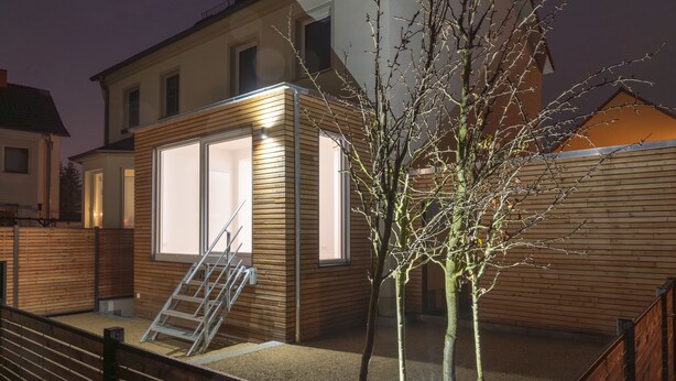 Una casa moderna con facciata in legno, una scala a vista e un albero nel giardino.