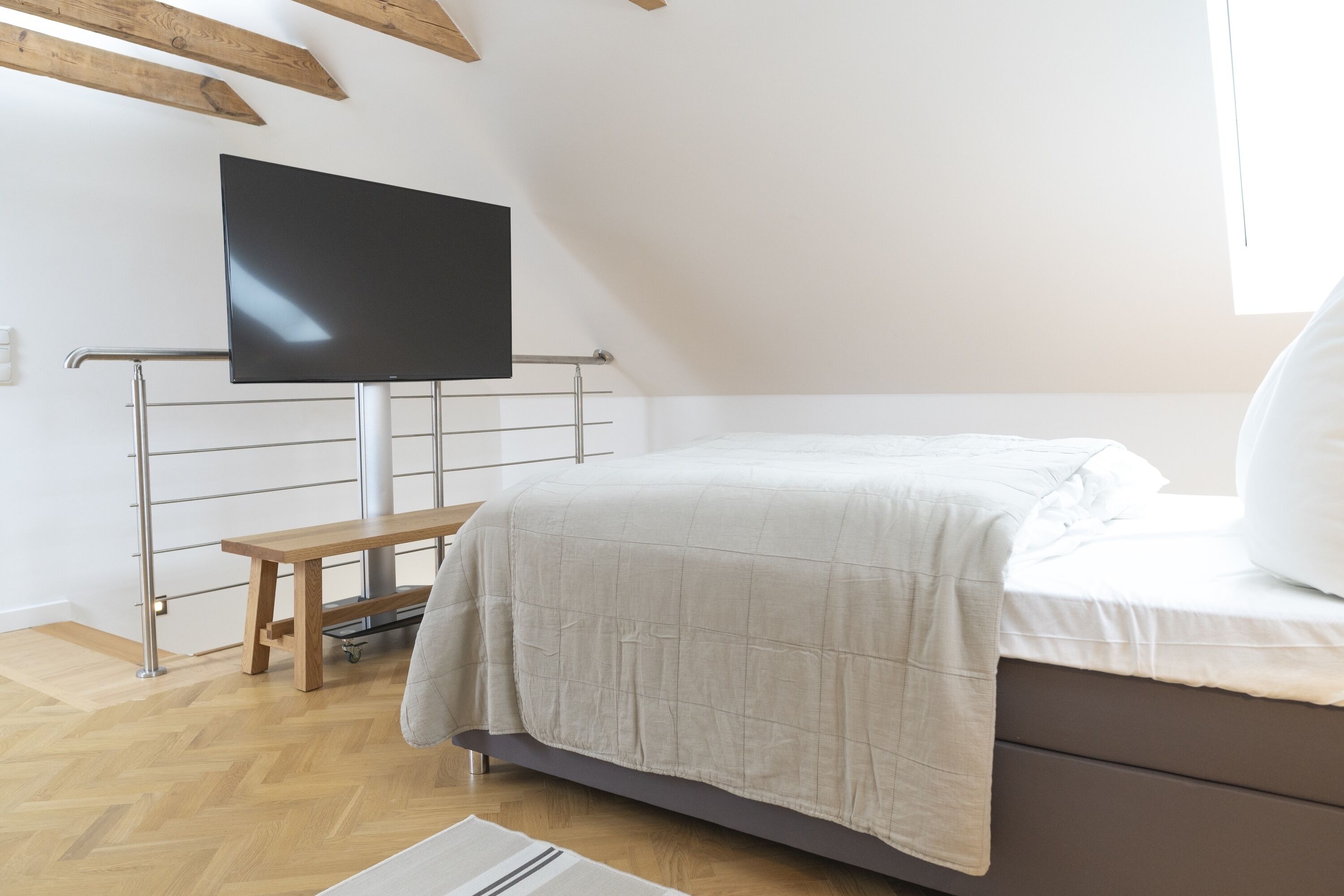 Une chambre à coucher avec un lit, un téléviseur fixé au mur, un banc en bois et une fenêtre.