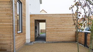 Un edificio moderno con pannelli in legno, un cortile in ghiaia e un vialetto che conduce a una porta.