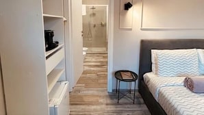 A bedroom with a bed, a small table, a wardrobe, and a shower area. - Camera ampia matrimoniale/tripla (Vitorchiano)