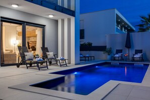 A modern outdoor pool area with lounge chairs and a well-lit patio. - Villa Martina Zadarvillas (Nin)