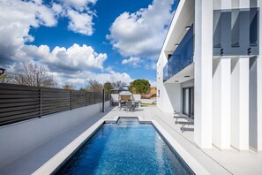 A modern outdoor pool area with a clear blue sky and a wooden fence. - Villa Martina Zadarvillas (Nin)