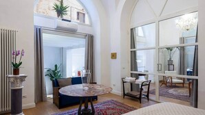 A spacious room with a round table, a large window with a view, and a balcony with plants.