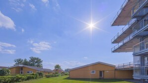 A modern building with a flat roof, a balcony on the upper floor, and a grassy area in front. - Ferienhaus in Rechlin (Rechlin)