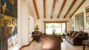 A spacious living room with high ceilings and wooden beams, featuring two leather sofas and a large painting on the wall. - Luxury Casa Guayllabamba - BBQ Jacuzzi Gym Piscina (Guayllabamba)