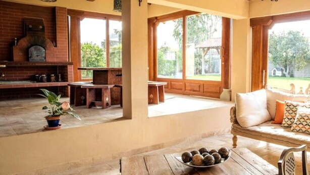 A spacious kitchen with a brick oven, wooden furniture, and large windows offering a view of the outdoors. - Luxury Casa Guayllabamba - BBQ Jacuzzi Gym Piscina (Guayllabamba)