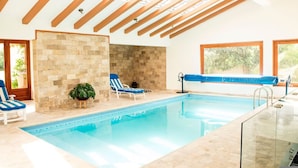 An indoor swimming pool with a stone wall, two lounge chairs, and a view of greenery outside. - Luxury Casa Guayllabamba - BBQ Jacuzzi Gym Piscina (Guayllabamba)