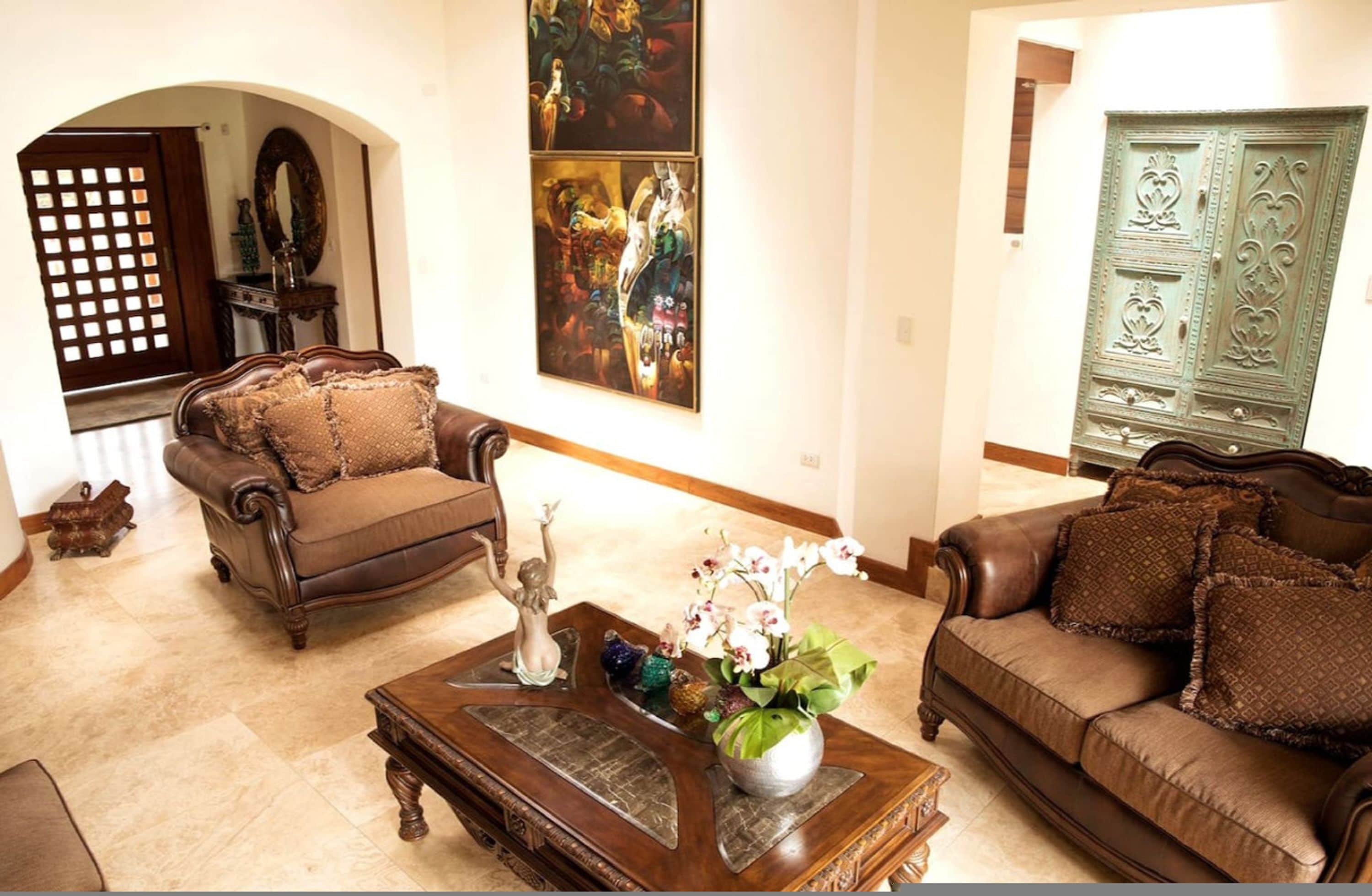 A living room with a brown sofa, a coffee table with decorative items, and a large painting on the wall.