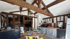 Una cuina rústica amb bigues de fusta, una taula de dinar amb caires grogues i un frigorífic blanc.