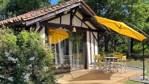 Una terrassa de fusta amb mobles d'exterior, un parasol groc i una porta de vidre que dóna a un pati.