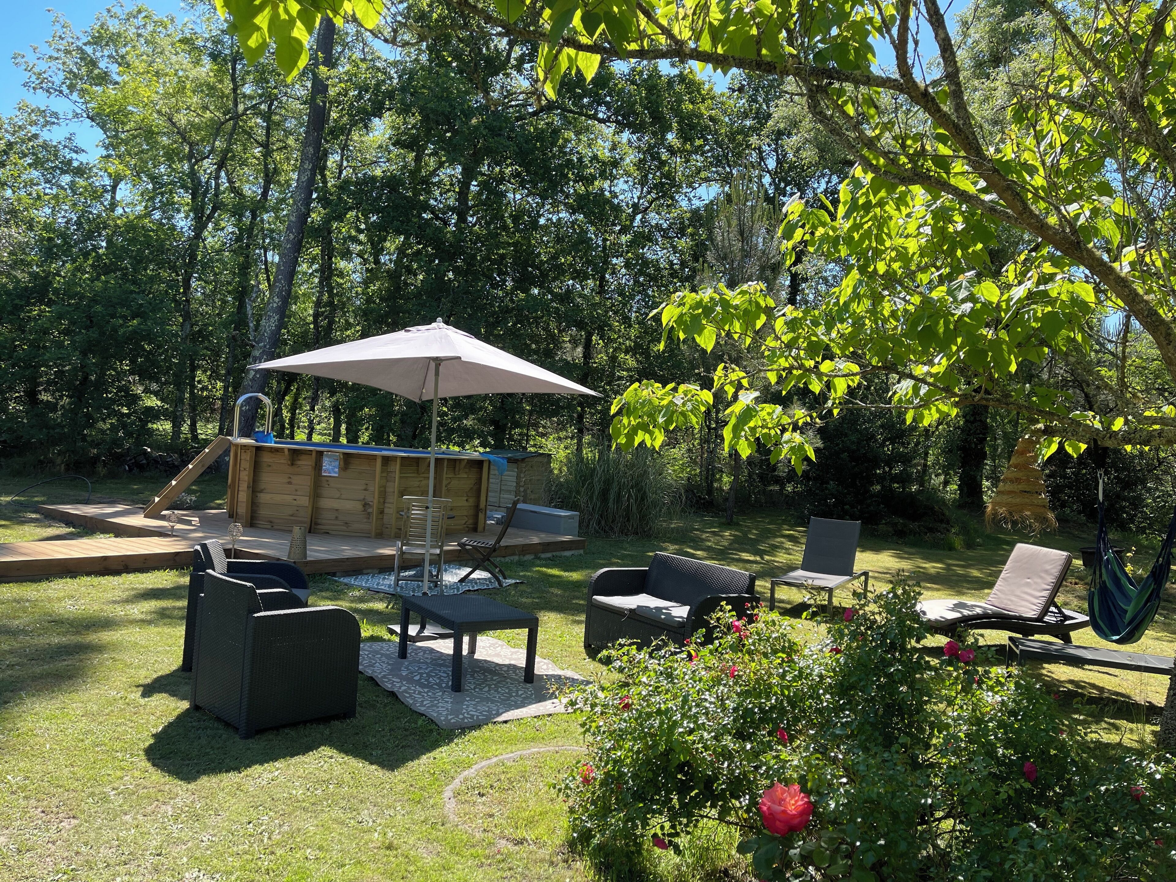 Une terrasse en bois avec des meubles d’extérieur, un jacuzzi et un grand parasol.
