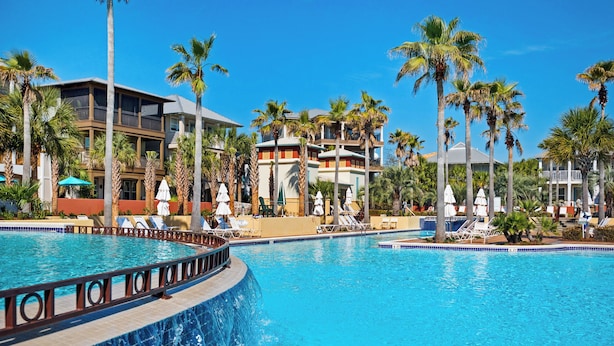 A resort with a large swimming pool, palm trees, and multiple buildings with balconies. - 4BR Seacrest Beach Home w/ Pool, Free Tram Service + Attraction Tickets! (Panama City Beach)