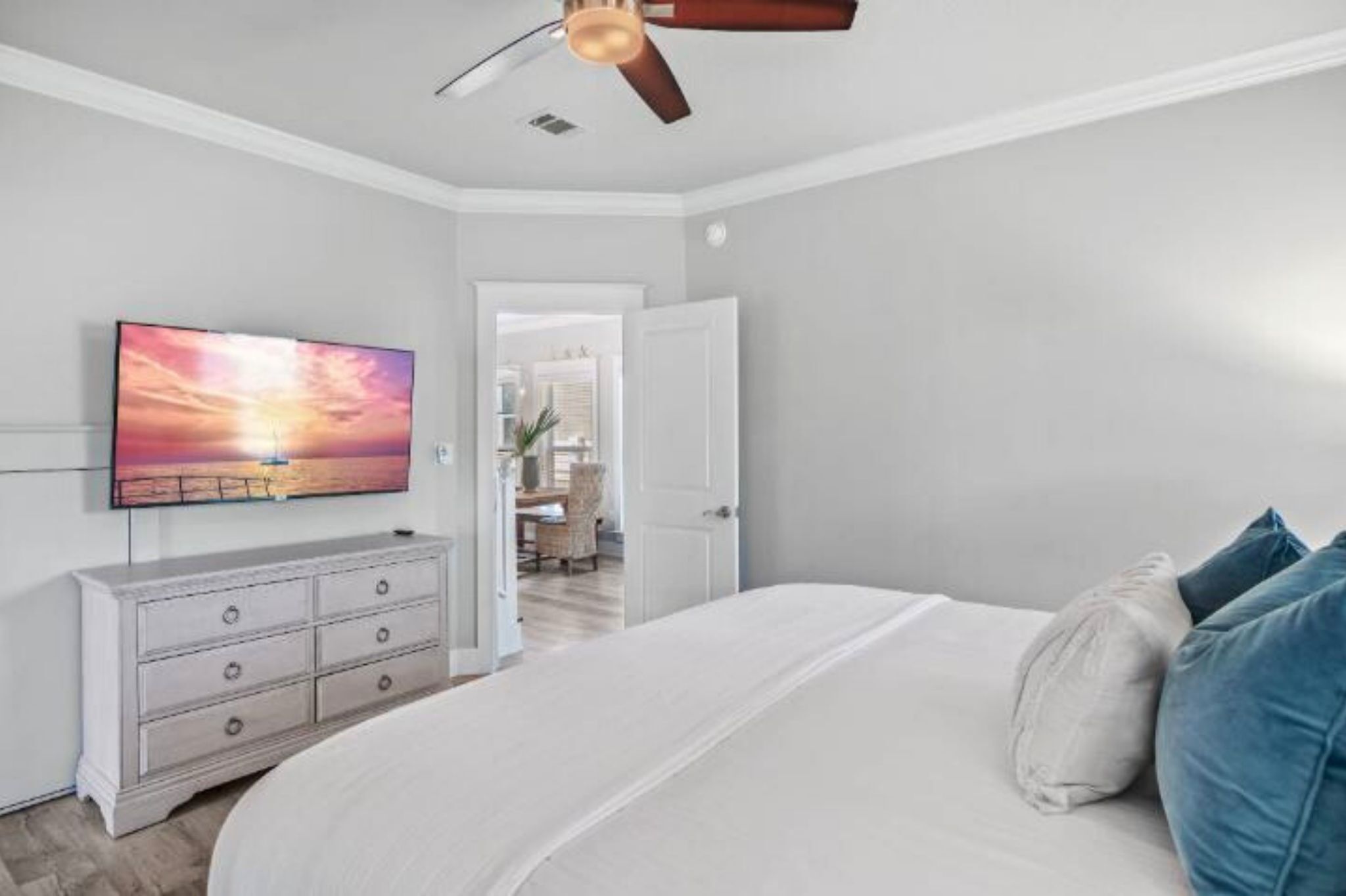 A bedroom with a bed, a dresser, a television, and a ceiling fan.