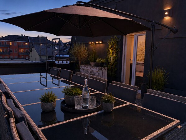An outdoor dining area with a table, chairs, a grill, and potted plants.