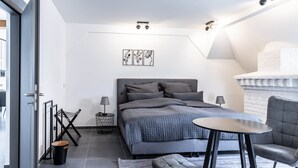 A modern bedroom with a bed, bedside tables, a chair, a small table, and a fireplace. - Familien Suite in Elbflorenz (Dresden)