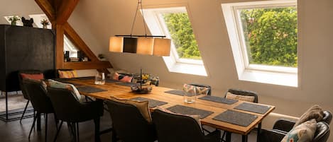 A dining area with a wooden table, black chairs, a hanging light fixture, and skylights.