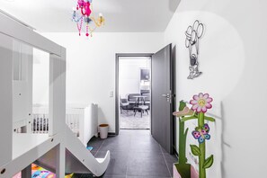 A modern interior with a white staircase, a hallway leading to a living area, and a door with a wall-mounted flower decoration. - Familien Suite in Elbflorenz (Dresden)