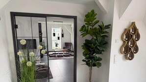 Un intérieur moderne avec une porte vitrée donnant sur un espace de vie, une grande plante en pot et des œuvres d’art décoratives au mur.