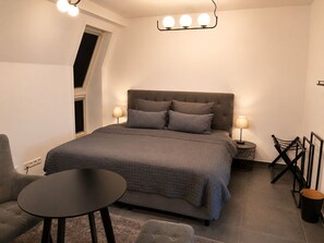 A bedroom with a bed, two bedside lamps, a round table, a chair, and a small table. - Familien Suite in Elbflorenz (Dresden)