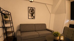 Un salon moderne comprenant un canapé, une table basse, un banc, une échelle sur laquelle sont posées des serviettes, une œuvre d’art murale et un luminaire suspendu.