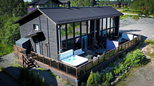 Une cabane moderne dotée d’une grande façade vitrée, d’un jacuzzi et d’une terrasse.