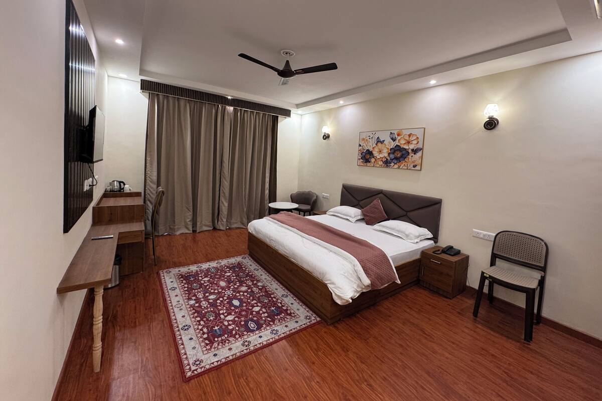 A modern bedroom with a bed, a desk, a chair, a ceiling fan, and a large window with curtains.