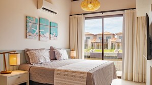 Un dormitorio con una cama grande, una mesita de noche, una lámpara y vistas a una piscina y edificios.