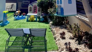 A backyard with artificial grass, a playhouse, a swing set, and a small table with chairs. - Family Design Villa & Play Garden near Sea, 3 BR, Sea Views (Chlorakas)