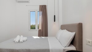 A neatly made bed with a headboard, a window with curtains, and a wall-mounted air conditioner.