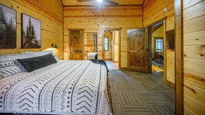 A wooden cabin bedroom with a bed, a ceiling fan, and a view of the hallway.
