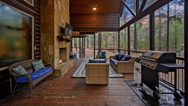 A covered outdoor deck with wicker furniture, a grill, and a stone fireplace.