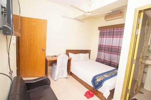A hotel room with a bed, a desk, a chair, a ceiling fan, and a bathroom. - Hotel D Palace (Dhaka)