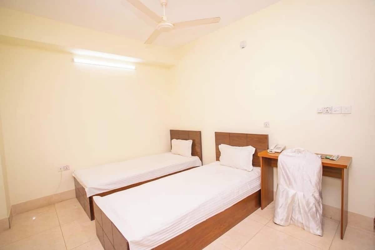 A room with two single beds, a desk with a telephone, and a ceiling fan.