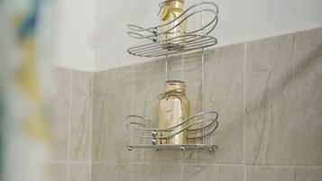 A bathroom with a shower, a towel rack, and a soap dispenser on a shelf.