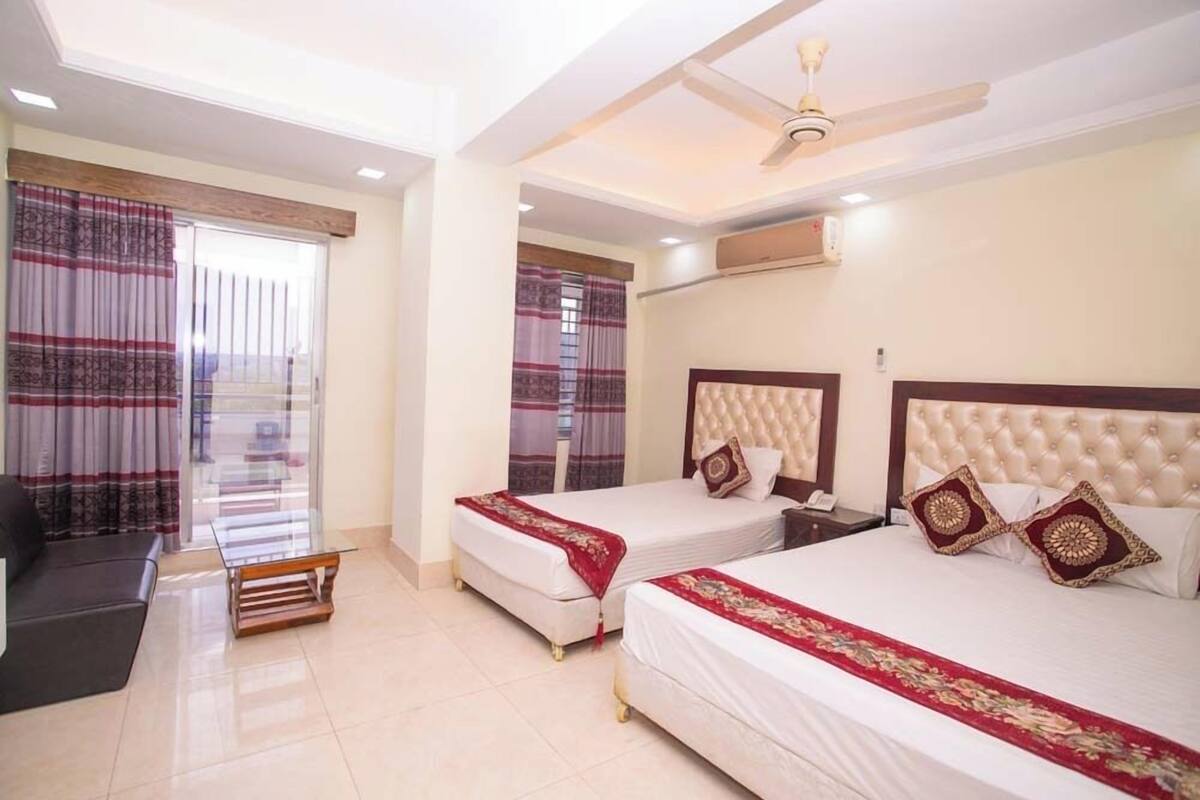 A hotel room with two beds, a sofa, a glass table, and a ceiling fan.