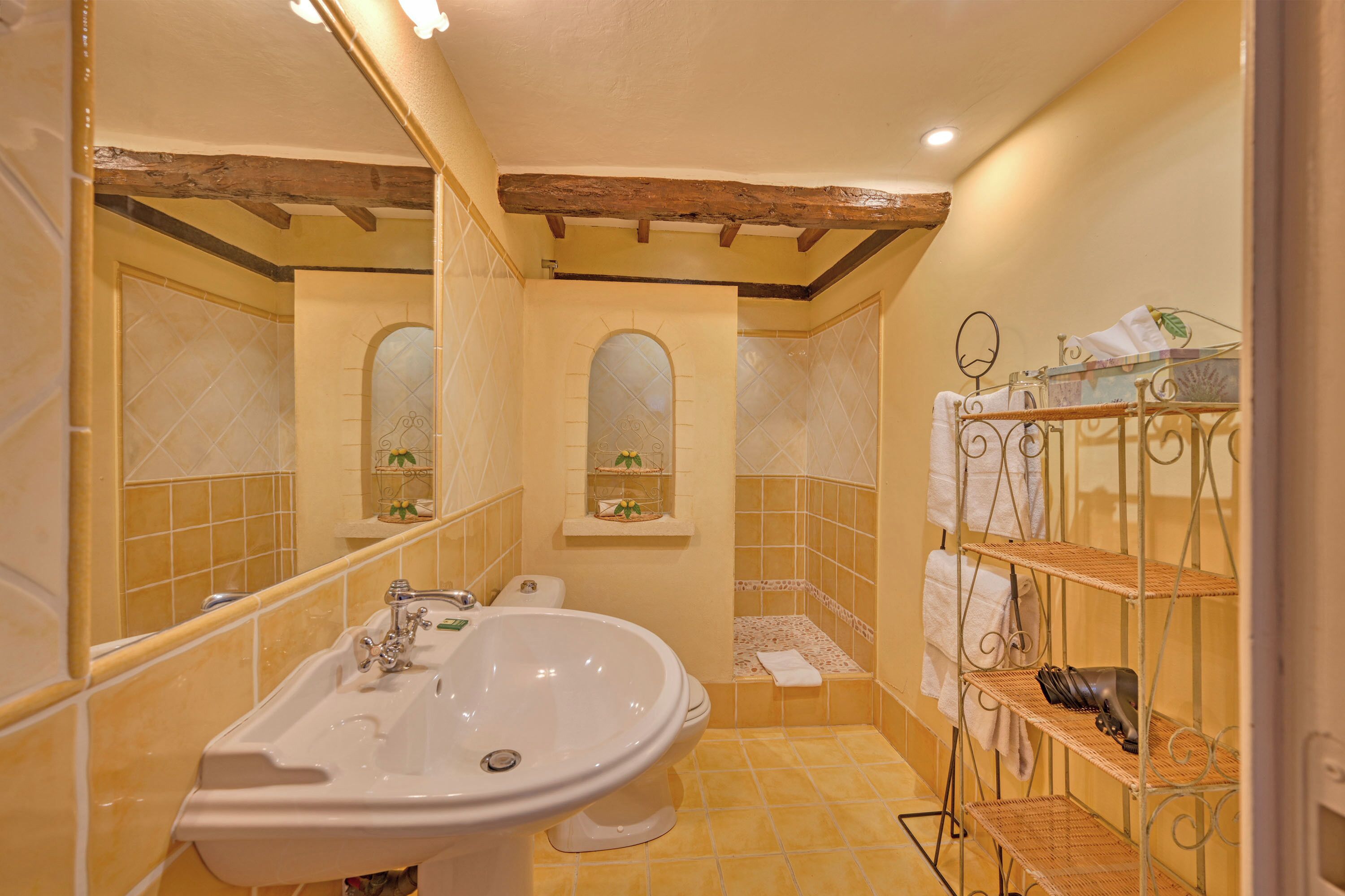 A bathroom with a sink, mirror, vanity, and shelves with towels and toiletries.