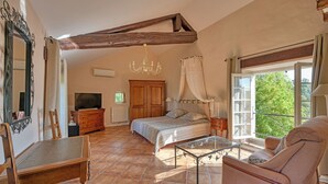 Une chambre à coucher avec un lit, une télévision, une armoire en bois, un lustre et un balcon avec vue.
