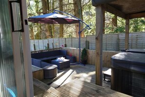 An outdoor patio area with a seating arrangement, a barbecue grill, and a wooden deck. - Wildwood Cabin - Sleeps 6, Hot Tub & Parking (Moffat)